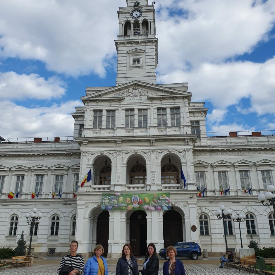 Piecas skolotājas nostājušās rindā, fonā Aradas rātsnams