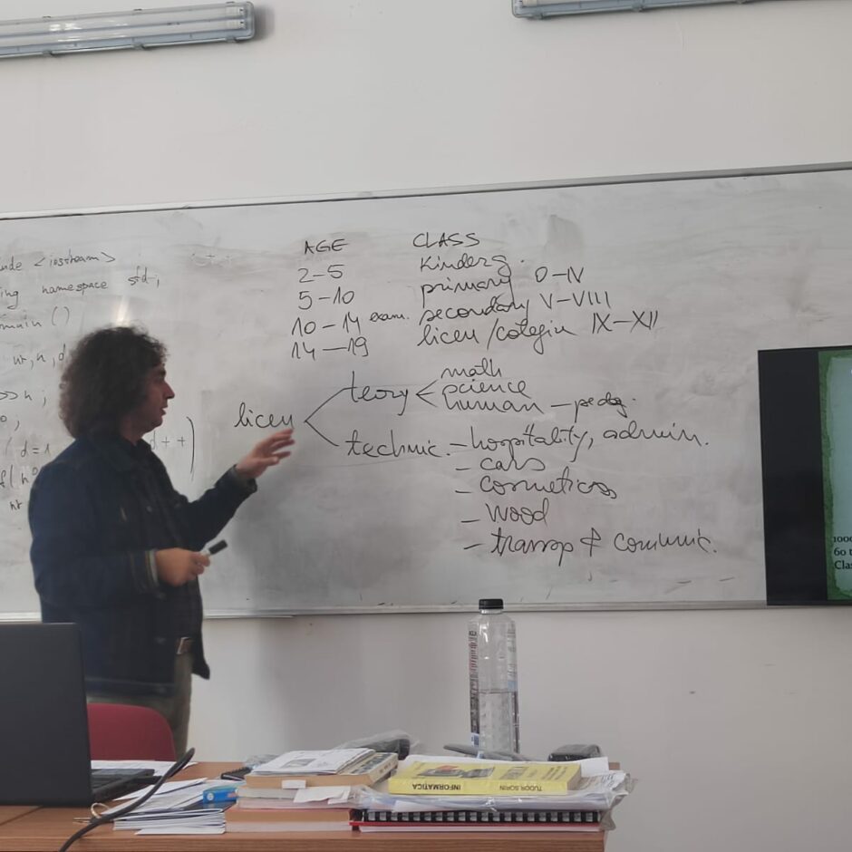 Skolotājs Marius Tiu stāsta par Rumānijas izglītības sistēmu, uz baltas tāfeles ar melnu marķieri raksta shēmu