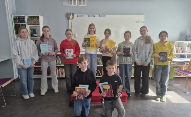 Attēlā redzami desmit divās rindās stāvoši 5.klašu skolēni, kuriem rokās ir diplomi un grāmatas.