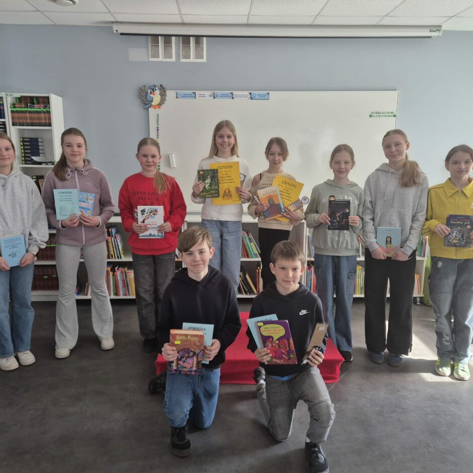 Attēlā redzami desmit divās rindās stāvoši 5.klašu skolēni, kuriem rokās ir diplomi un grāmatas.