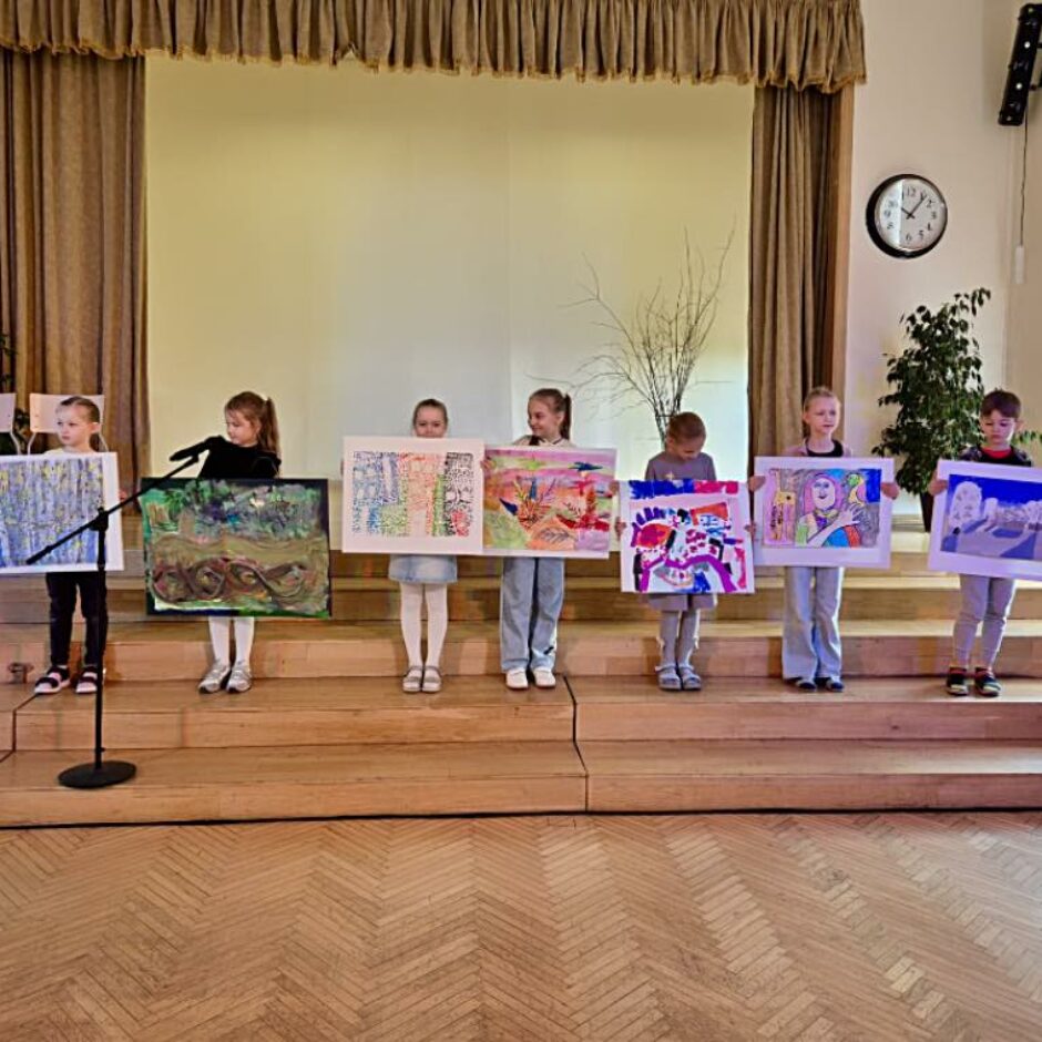 Attēlā redzami septiņi 1.klašu skolēni, kuri rāda savus uzzīmētos darbiņus uz A3 lapām