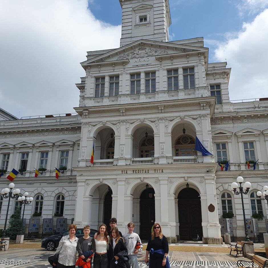 Attēlā redzama 7.klases piecu skolēnu un divi skolotāju grupa pie ēkas Rumānijā