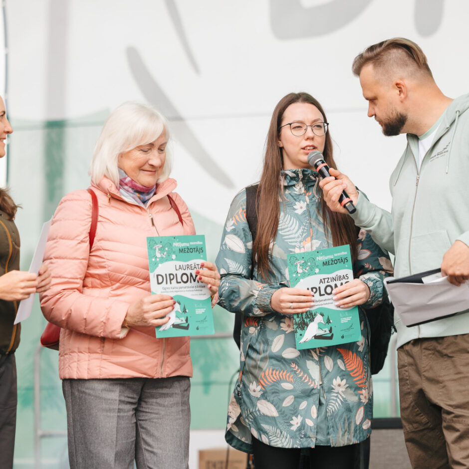 Attēlā redzamas skolotājas saņemot atzinības rakstus no pasākuma organizatora