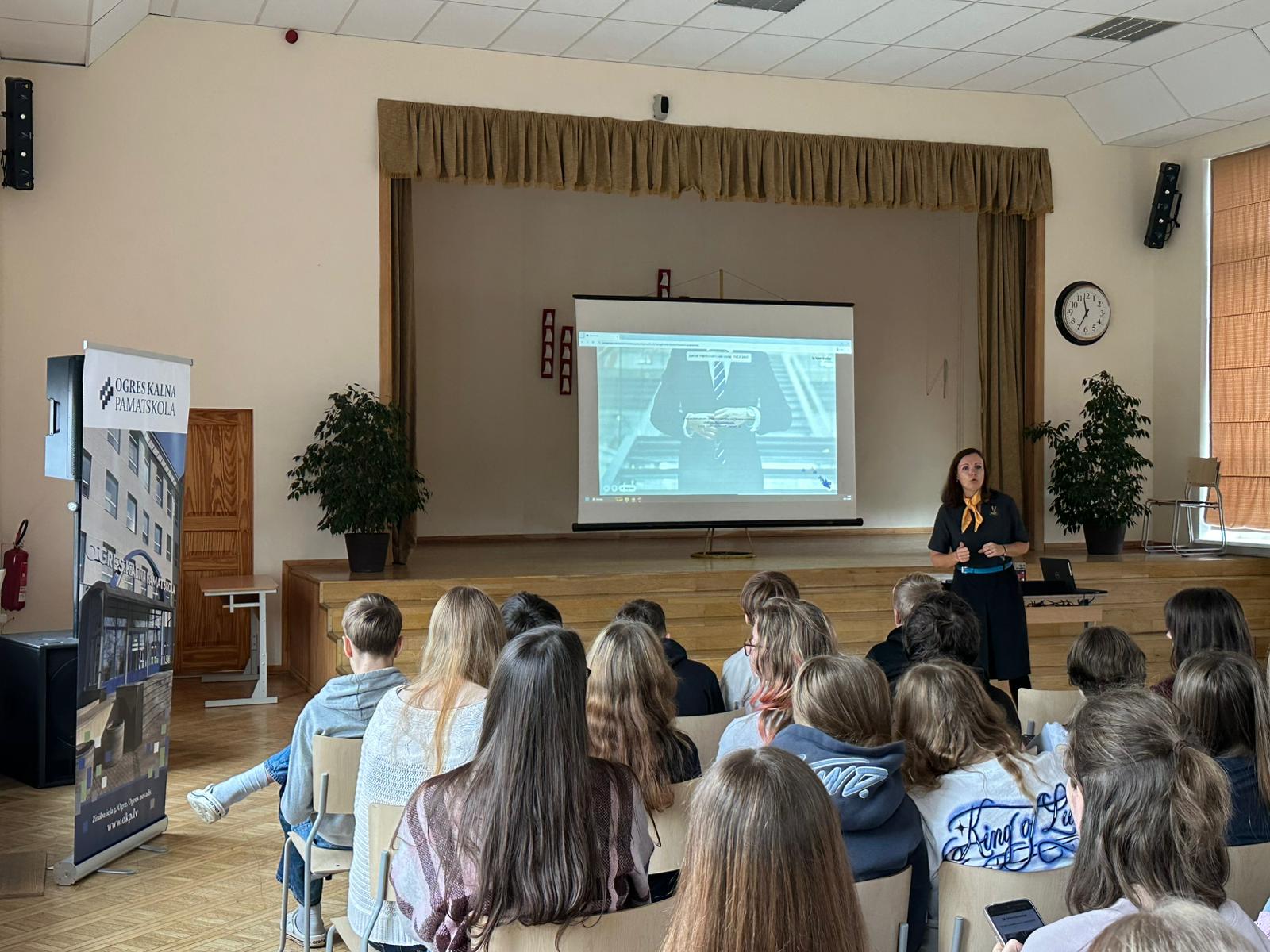 Lektore skolas Lielajā zālē vada skolēniem lekciju