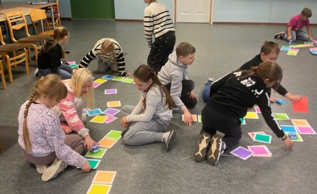 Skolēnu grupa veic uzdevumu uz grīdas ar krāsainām kartītēm