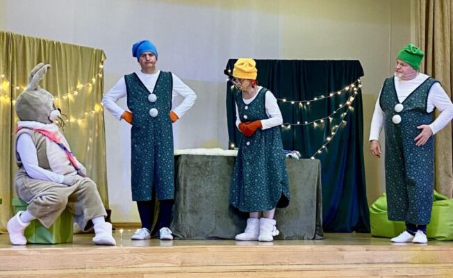 Aktieri rūķu tērpos uz skatuves izrādē “Pasaku sargi” skolas Lielajā zālē