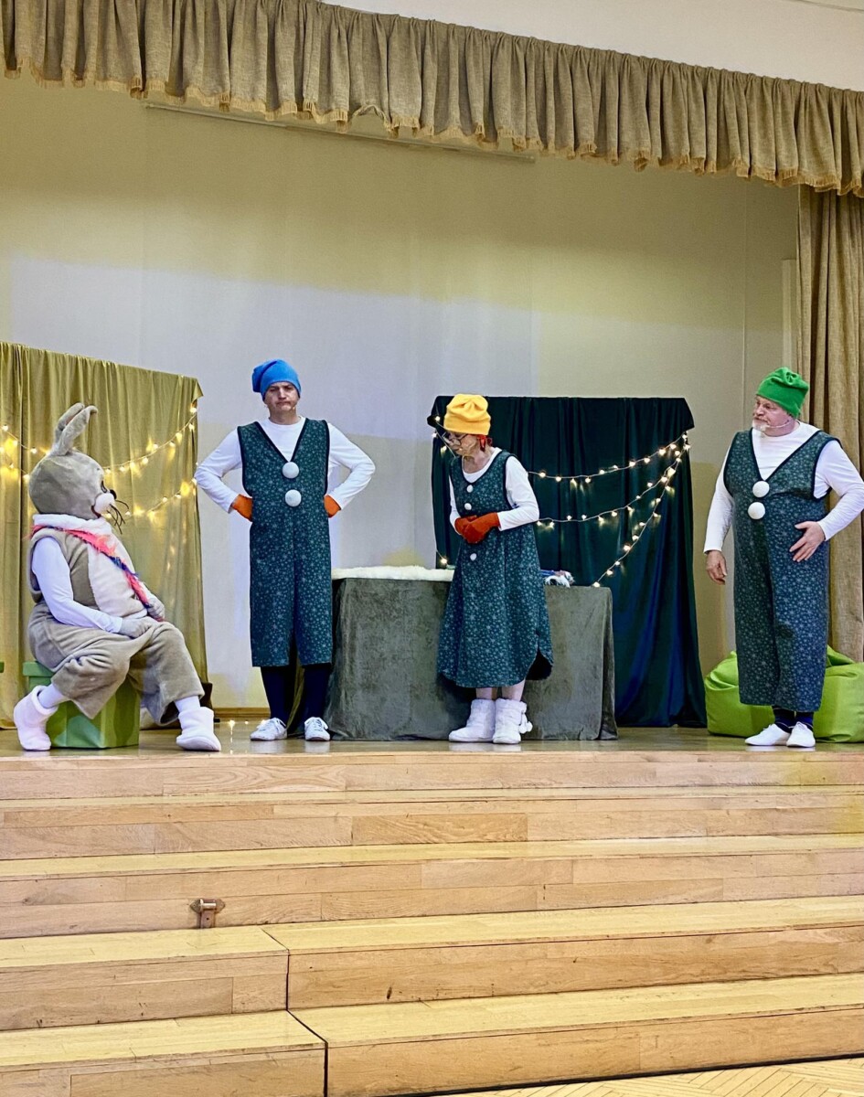 Aktieri rūķu tērpos uz skatuves izrādē “Pasaku sargi” skolas Lielajā zālē