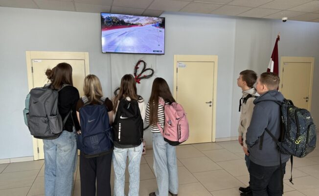 Skolēnu grupa skatās TV pārraidi no Olimpiādes skolas foajē televizorā