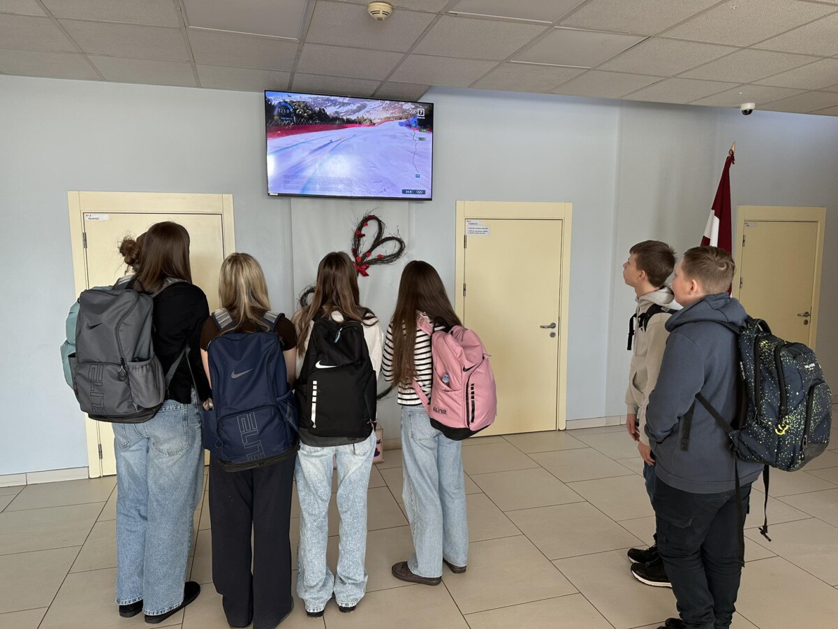 Skolēnu grupa skatās TV pārraidi no Olimpiādes skolas foajē televizorā