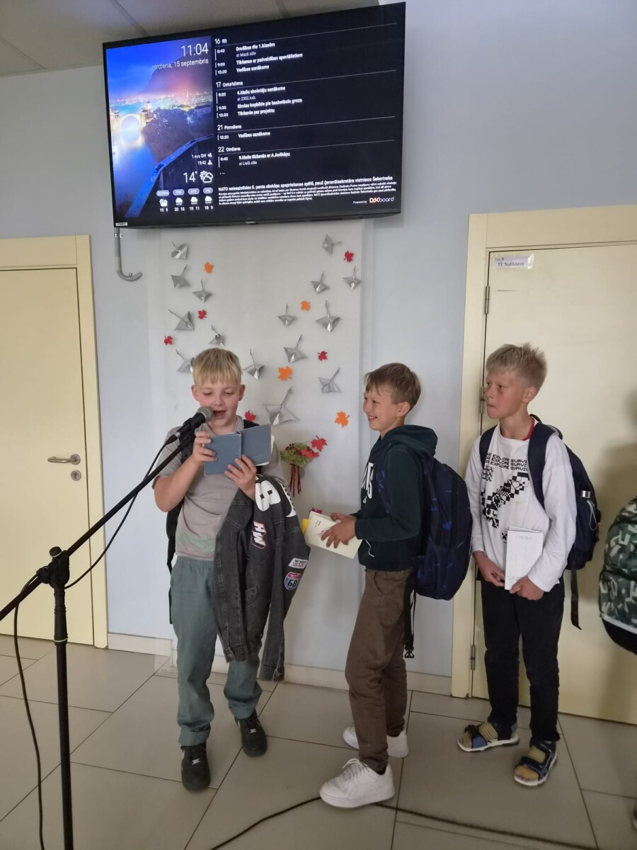 Trīs skolēni pie mikrofona lasa dzeju.